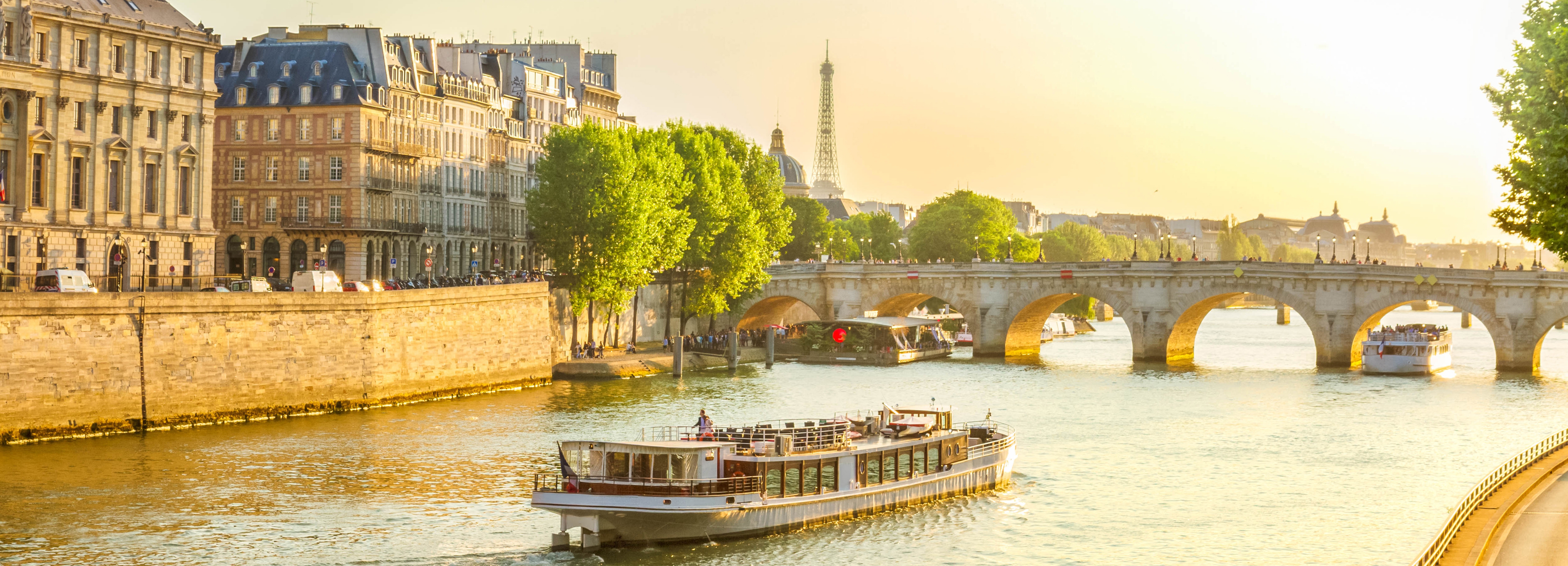 Udsigt over Pont Neuf broen og Seinen i Paris med et flodkrydstogt i solnedgangen og Eiffeltårnet i baggrunden