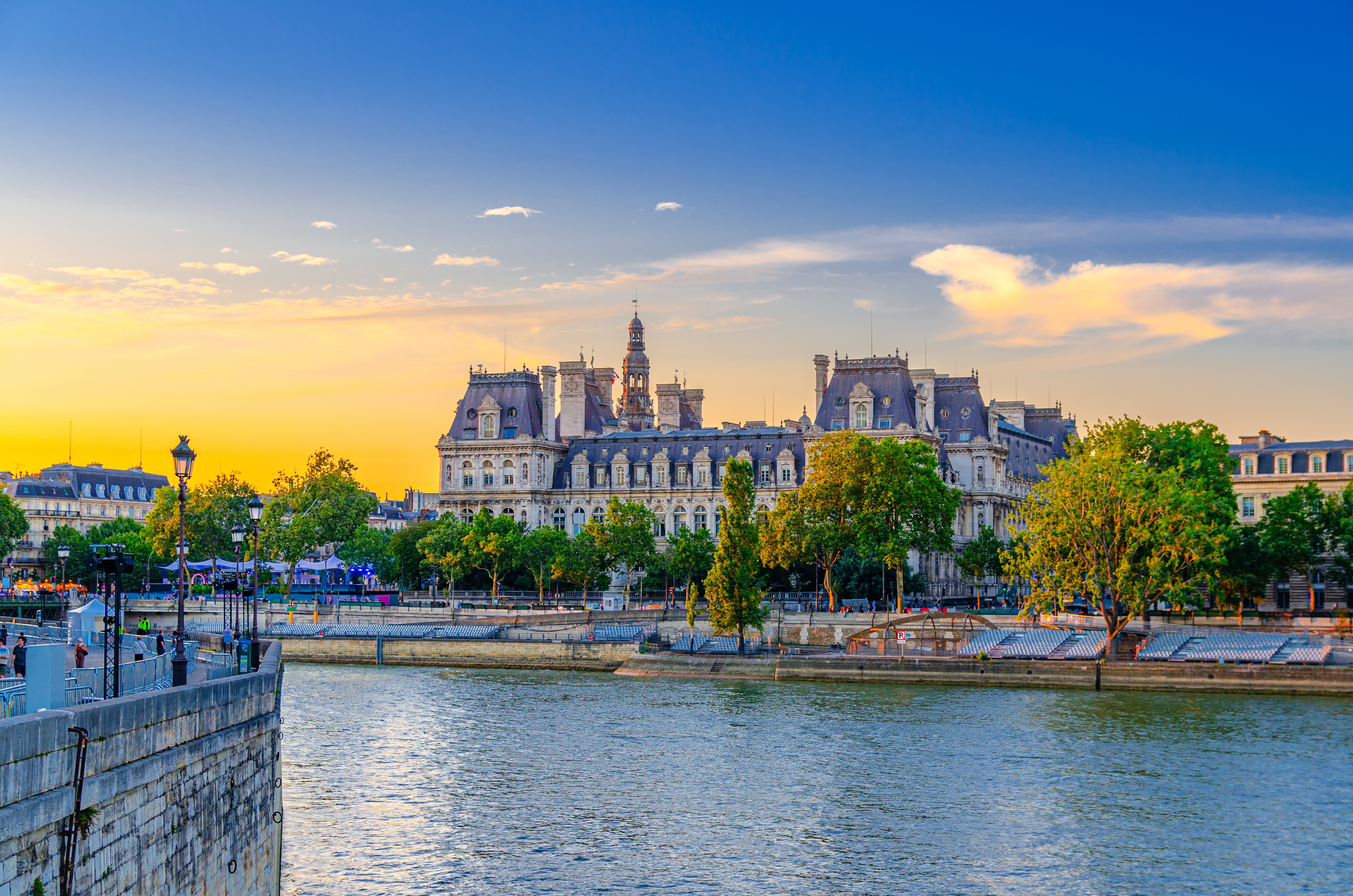 Romantisk aftenudsigt over Paris med Hotel de Ville og Seine-floden badet i gyldent solnedgangslys, perfekt til en storbyferie i Frankrigs hovedstad