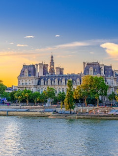 Romantisk aftenudsigt over Paris med Hotel de Ville og Seine-floden badet i gyldent solnedgangslys, perfekt til en storbyferie i Frankrigs hovedstad