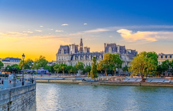 Romantisk aftenudsigt over Paris med Hotel de Ville og Seine-floden badet i gyldent solnedgangslys, perfekt til en storbyferie i Frankrigs hovedstad