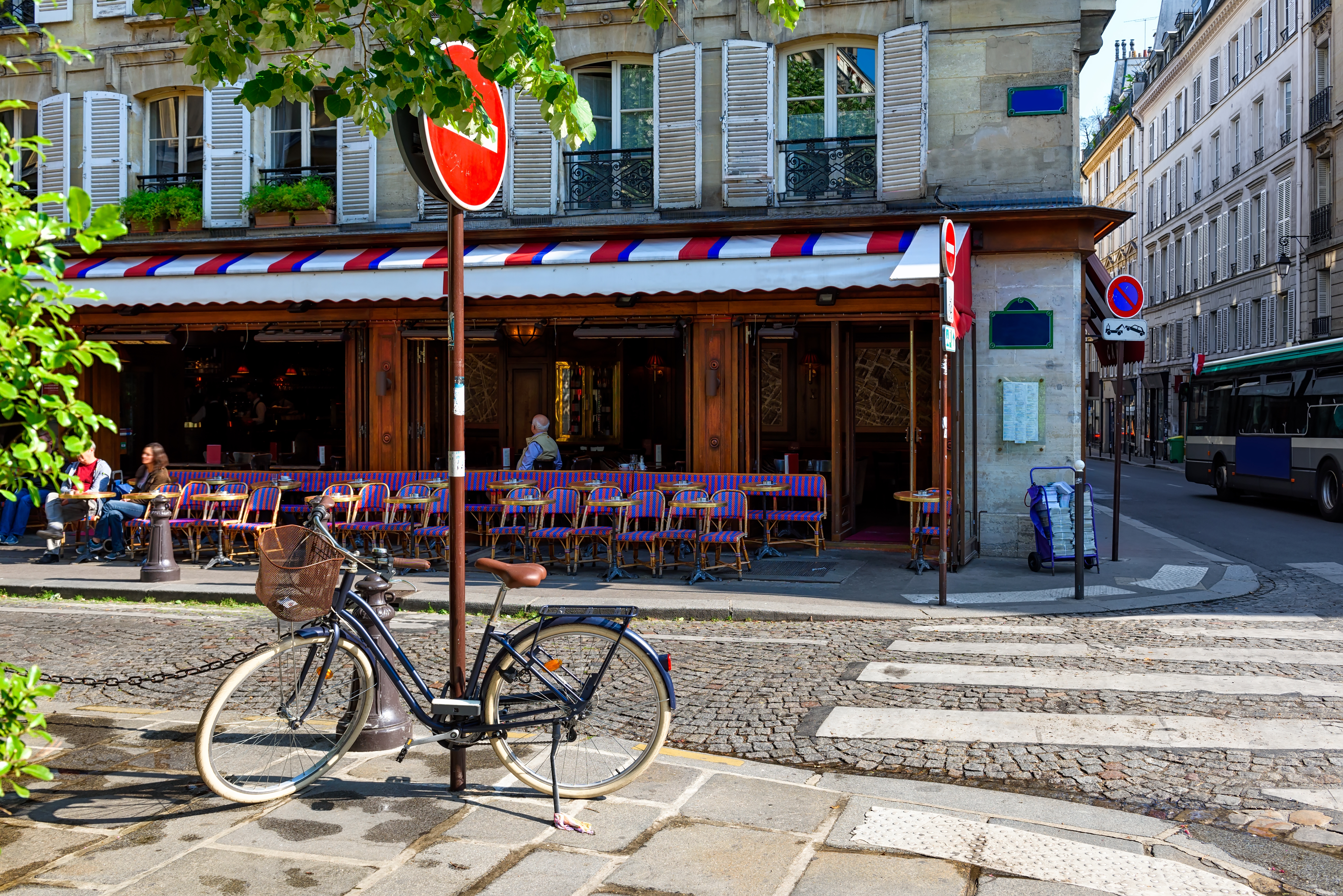 Hyggelig café terrasse i Paris med rød-hvid-blå markise, lilla stole og en cykel parkeret på brolagt gade i Frankrig