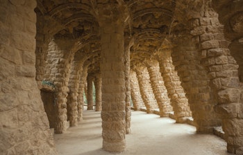Rustikke stensøjler og buer i Park Güell, Barcelona, der viser Antoni Gaudís unikke arkitektoniske stil med naturlige materialer og organiske former