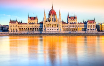 Den ikoniske parlamentsbygning i Budapest badet i gyldent solnedgangslys med smukke refleksioner i Donau-floden
