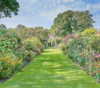Smuk engelsk have ved Pashley Manor Gardens med farverige blomsterborde langs en grøn græsgang der fører mod det historiske herregårdsanlæg