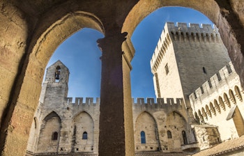 Pavepaladset i Avignon set gennem historiske stenbuer med imponerende middelalderarkitektur og tårne mod blå himmel