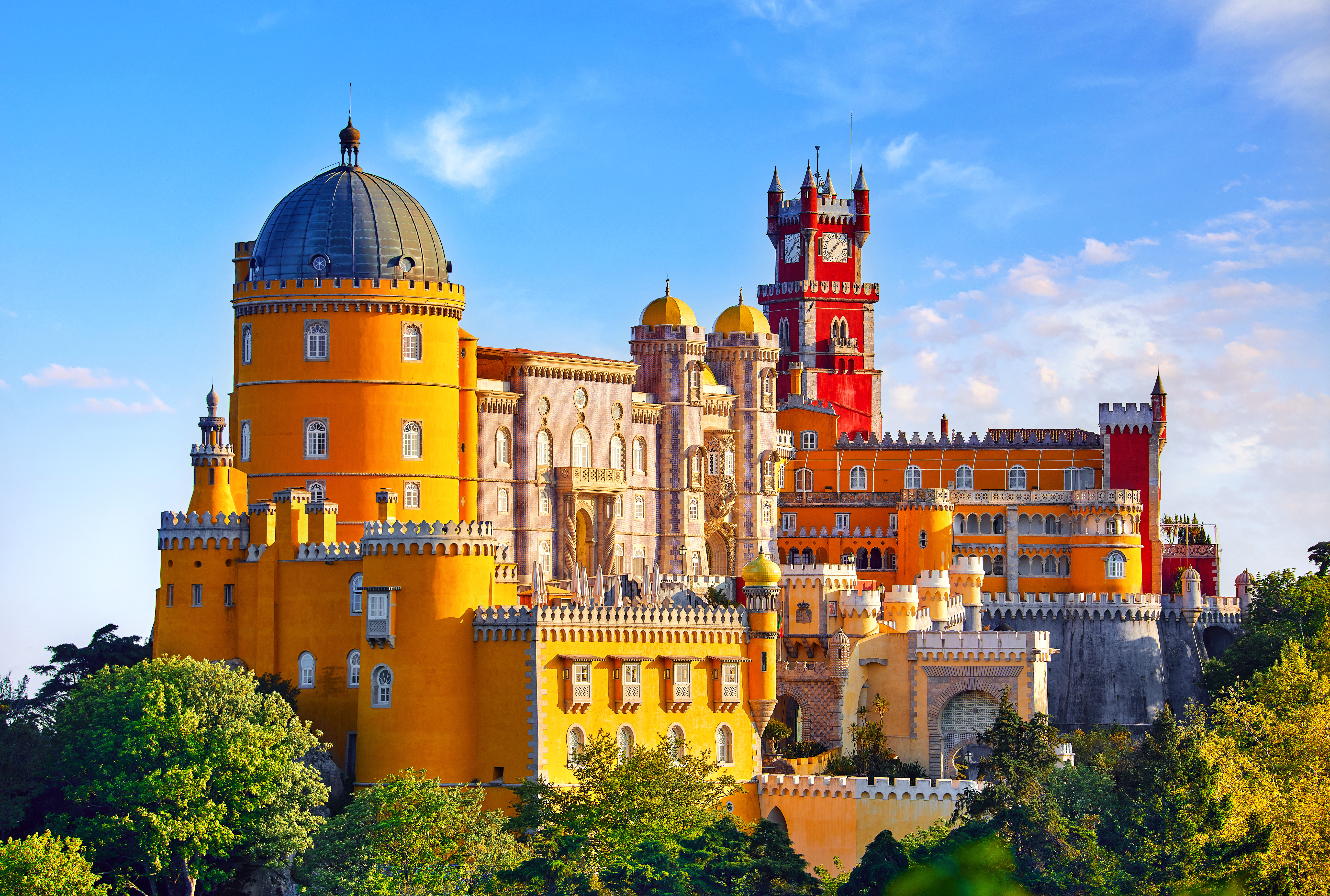 Farverigt Pena Palads med taarne og kupler i Sintra Portugal omgivet af groenne traeer