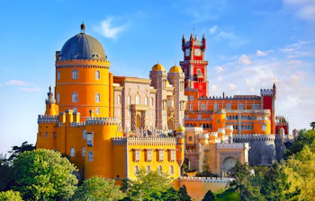 Farverigt Pena Palads med taarne og kupler i Sintra Portugal omgivet af groenne traeer