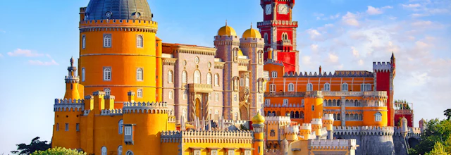 Farverigt Pena Palads med taarne og kupler i Sintra Portugal omgivet af groenne traeer