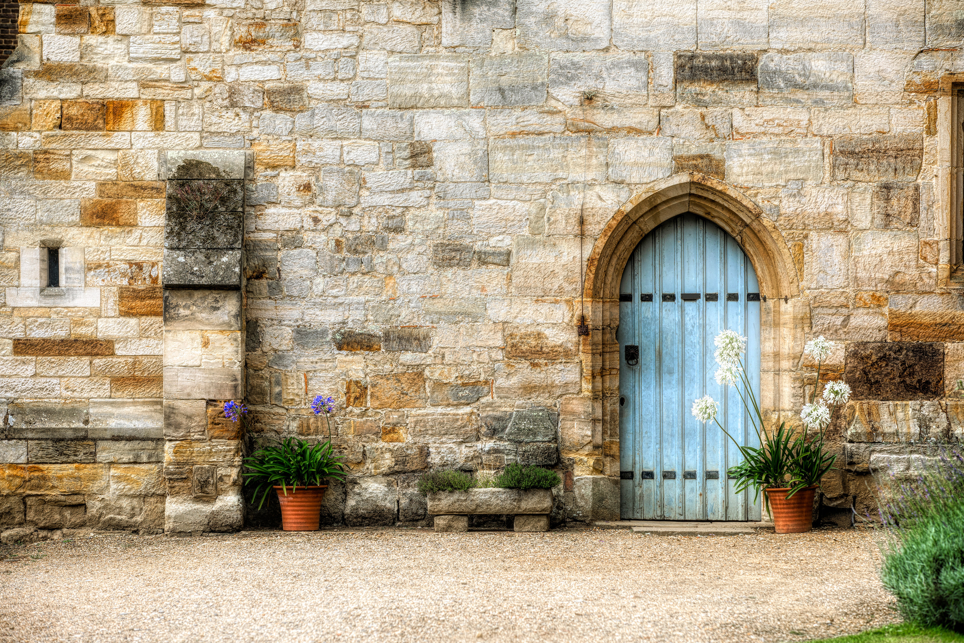 Charmerende blå buet dør med blomsterkrukker ved den historiske stenfacade på Penshurst Place herregård i Kent, England