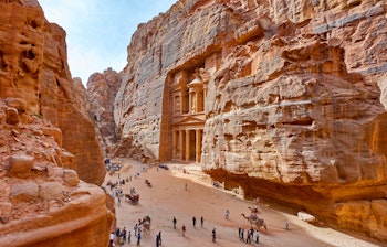 Det spektakulære Treasury tempel hugget ud i de røde klippevægge i Petra, Jordan med turister der udforsker det antikke arkæologiske verdensarvsted