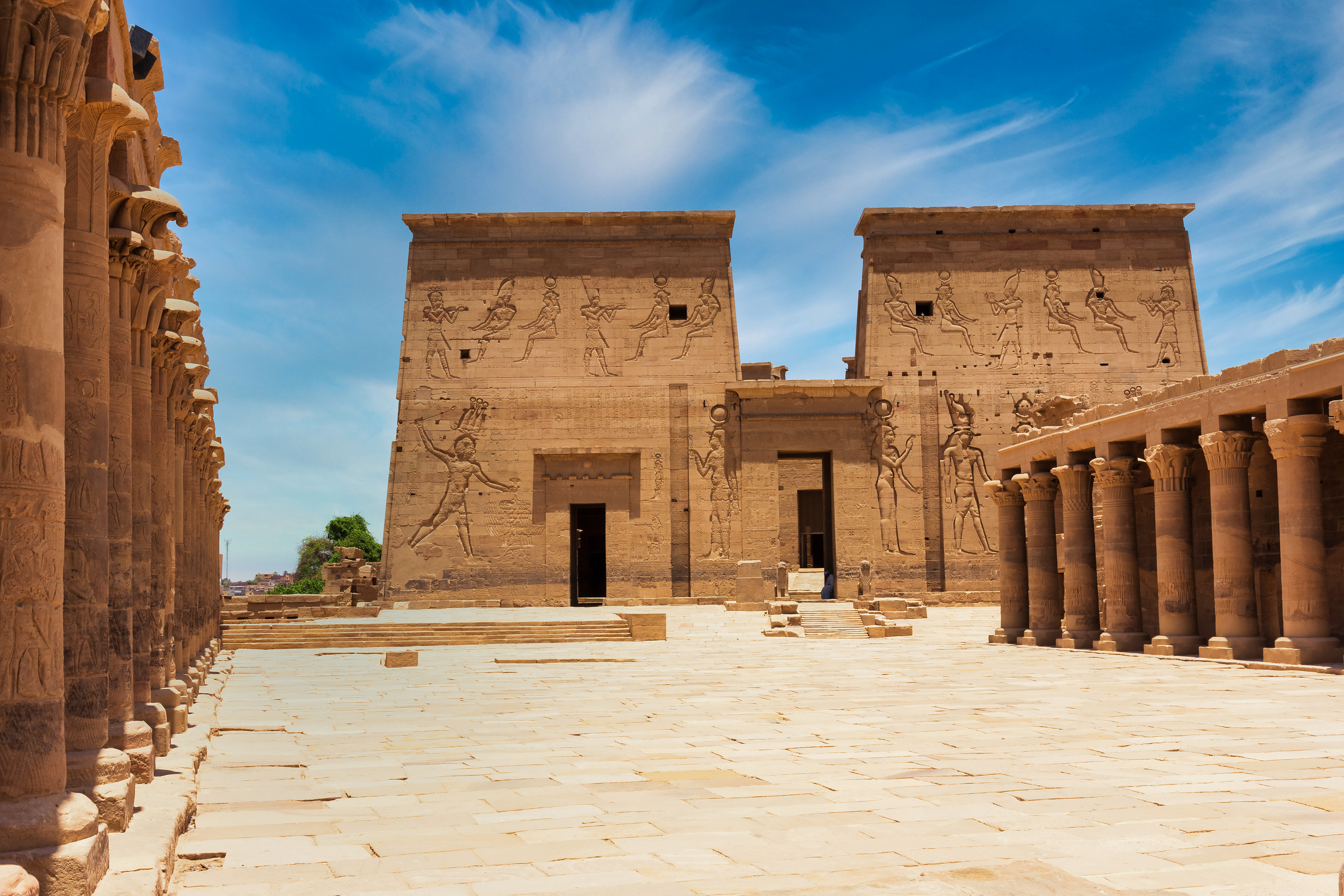Den imponerende første pylon ved Philae-templet på Agilkia-øen i Aswan, Egypten, prydet med hieroglyffer og flankeret af dekorerede søjler under en klar blå himmel