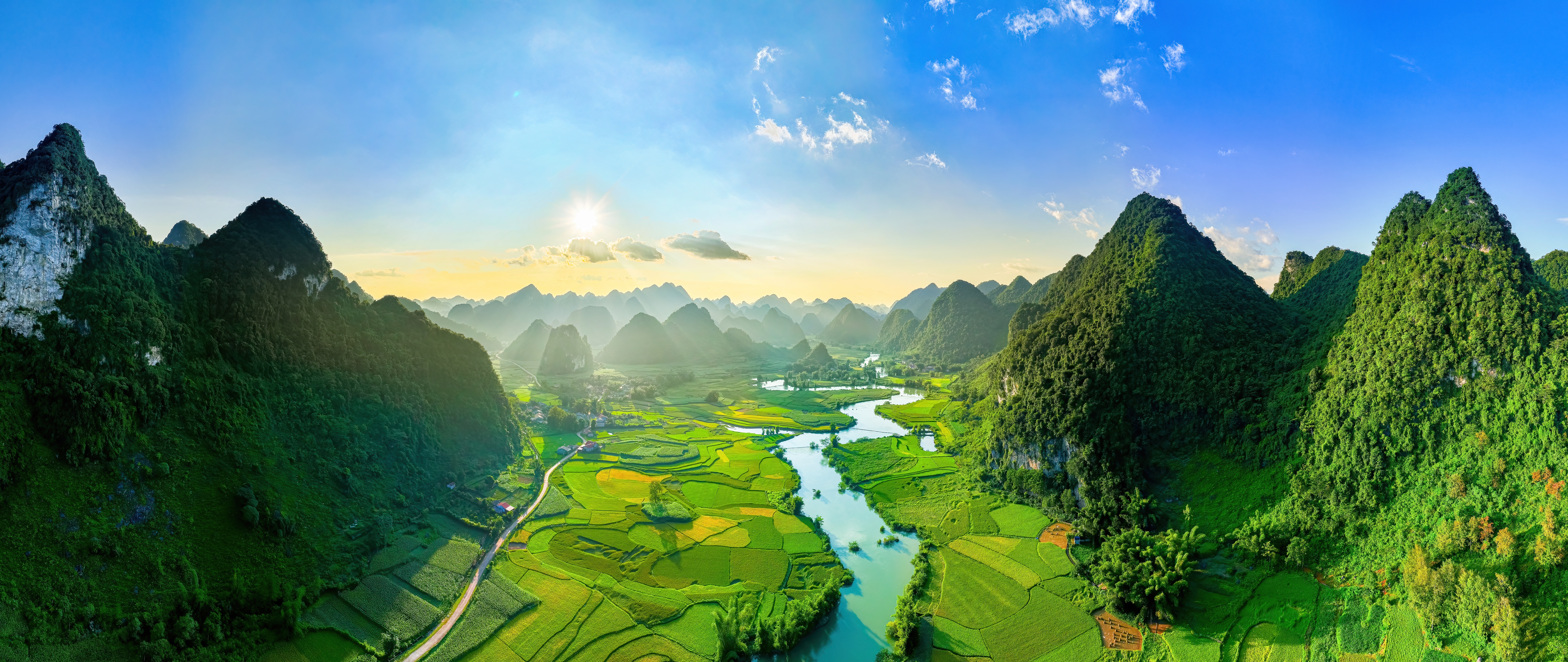 Luftfoto af Phong Nam-dalen ved solnedgang med slyngede flod gennem grønne rismarker og dramatiske kalkstensbjerg i Cao Bang-provinsen, det nordlige Vietnam