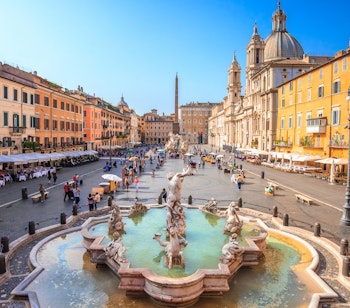 Luftfoto af Piazza Navona i Rom ved skumringstid med barokke springvand og bygninger fra det antikke Stadium of Domitian oplyst under en blå himmel