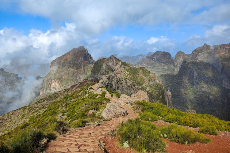 Dramatisk bjergsti mellem Pico do Arieiro og Pico Ruivo på Madeira i 1818 meters højde, med klippeformationer og skyer der omgiver de majestætiske bjergtinder