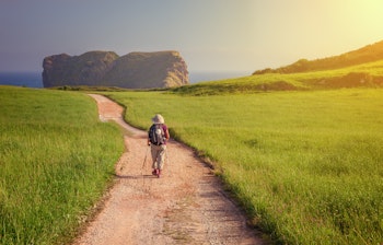 Pilgrimsvandrer på vej mod Sankt Martin kirken ved kysten i Llanes med udsigt til Camaras-stranden, Caminoen, Asturien, Spanien
