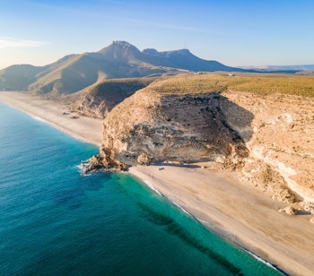 Betagende solopgang over Playa de los Muertos stranden med krystalklart turkisblåt vand og hvidt sand omgivet af klippeformationer i Cabo de Gata naturpark, Almeria, Spanien