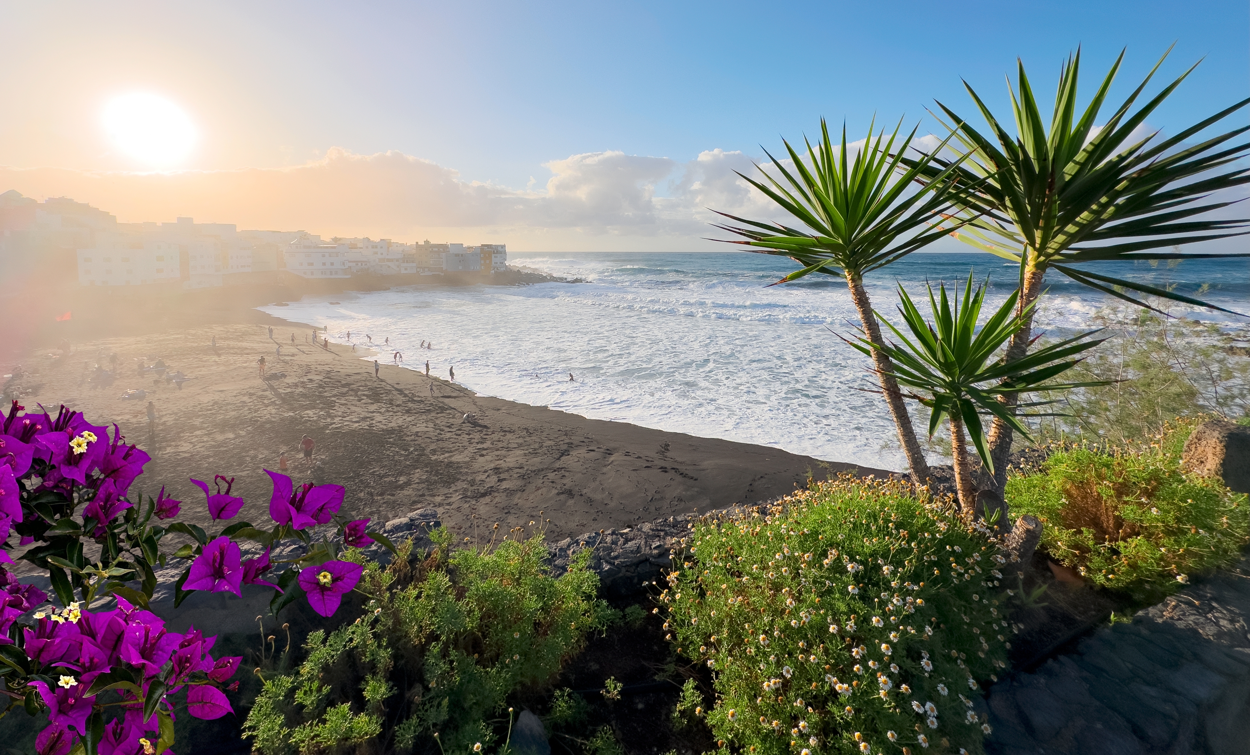 Den smukke Playa Jardin strand med sort vulkansk sand og vajende palmer i Puerto de la Cruz på Tenerife, med udsigt til den charmerende kystby og det azurblå Atlanterhav