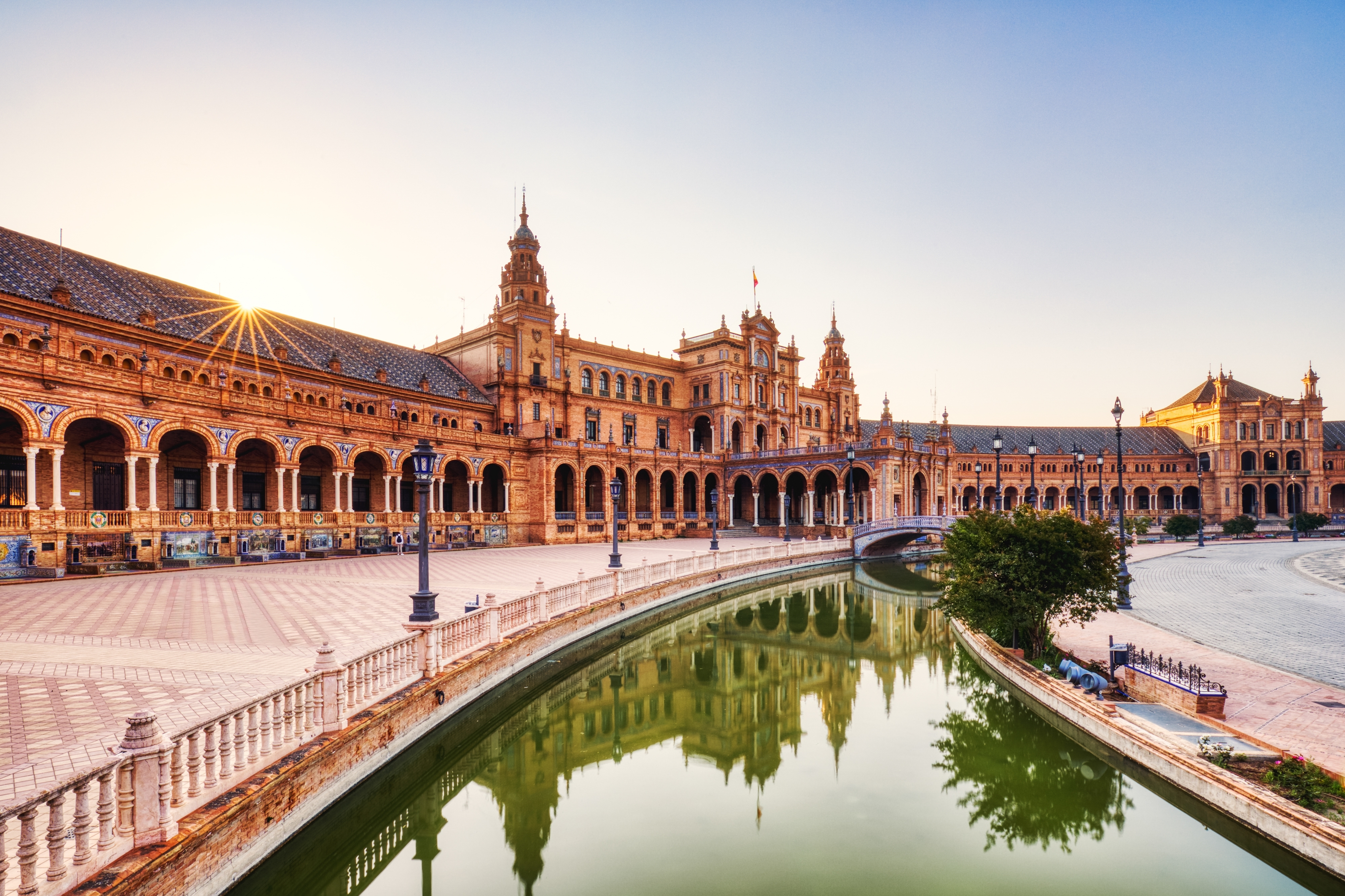 Smuk solnedgang over Plaza de España i Sevilla med gyldent lys på den historiske arkitektur, buer og vandkanal
