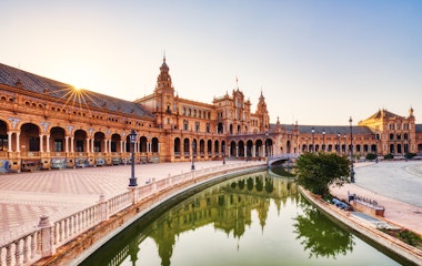 Smuk solnedgang over Plaza de España i Sevilla med gyldent lys på den historiske arkitektur, buer og vandkanal