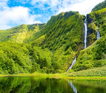 Betagende udsigt over Poço da Ribeira do Ferreiro vandfald og lagune omgivet af frodig grøn skov på Flores-øen, Azorerne, Portugal
