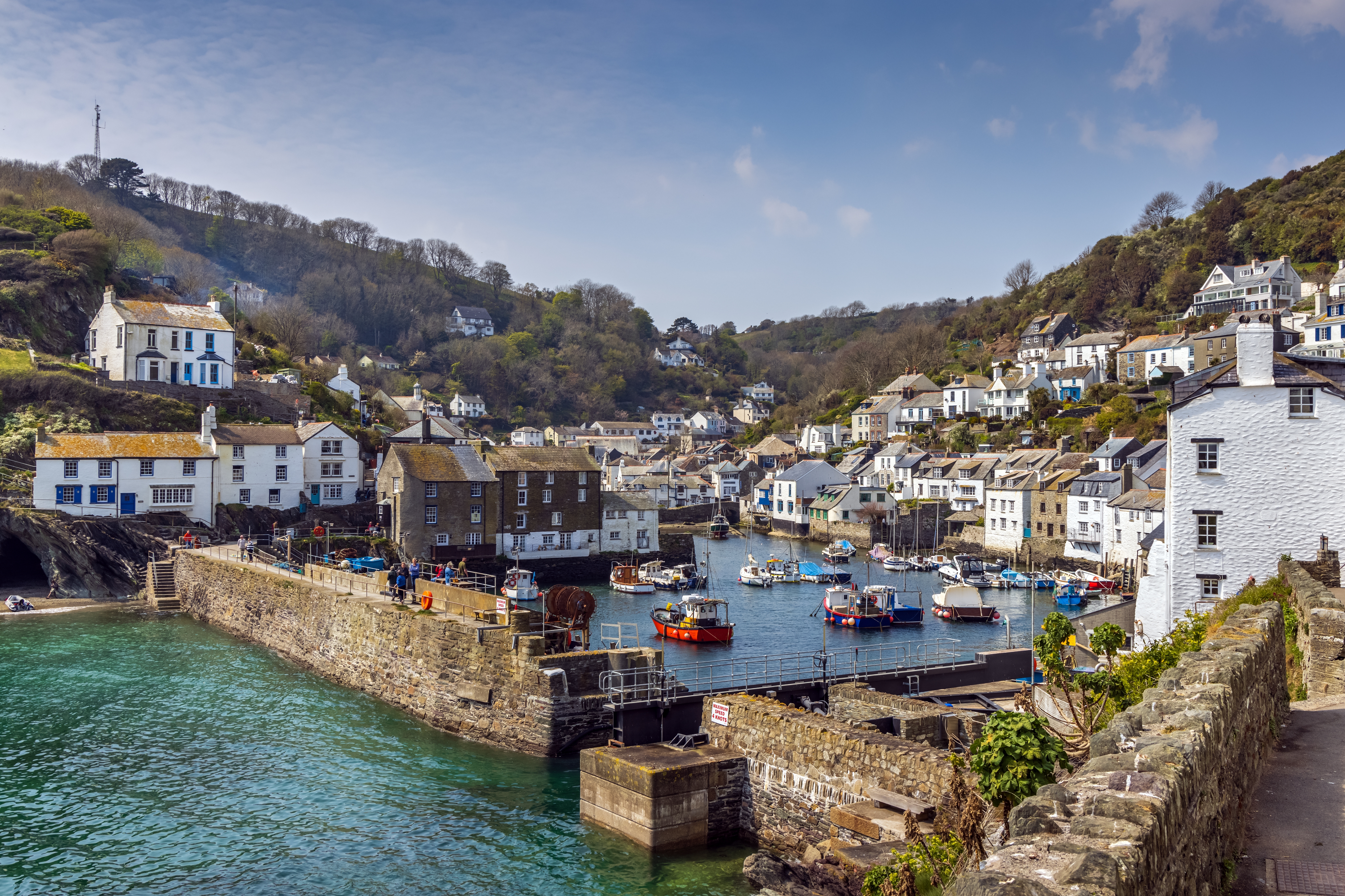Den charmerende indgang til den historiske fiskerlandsby Polperro med farverige huse og både i havnen på en solrig sommerdag i Cornwall, England