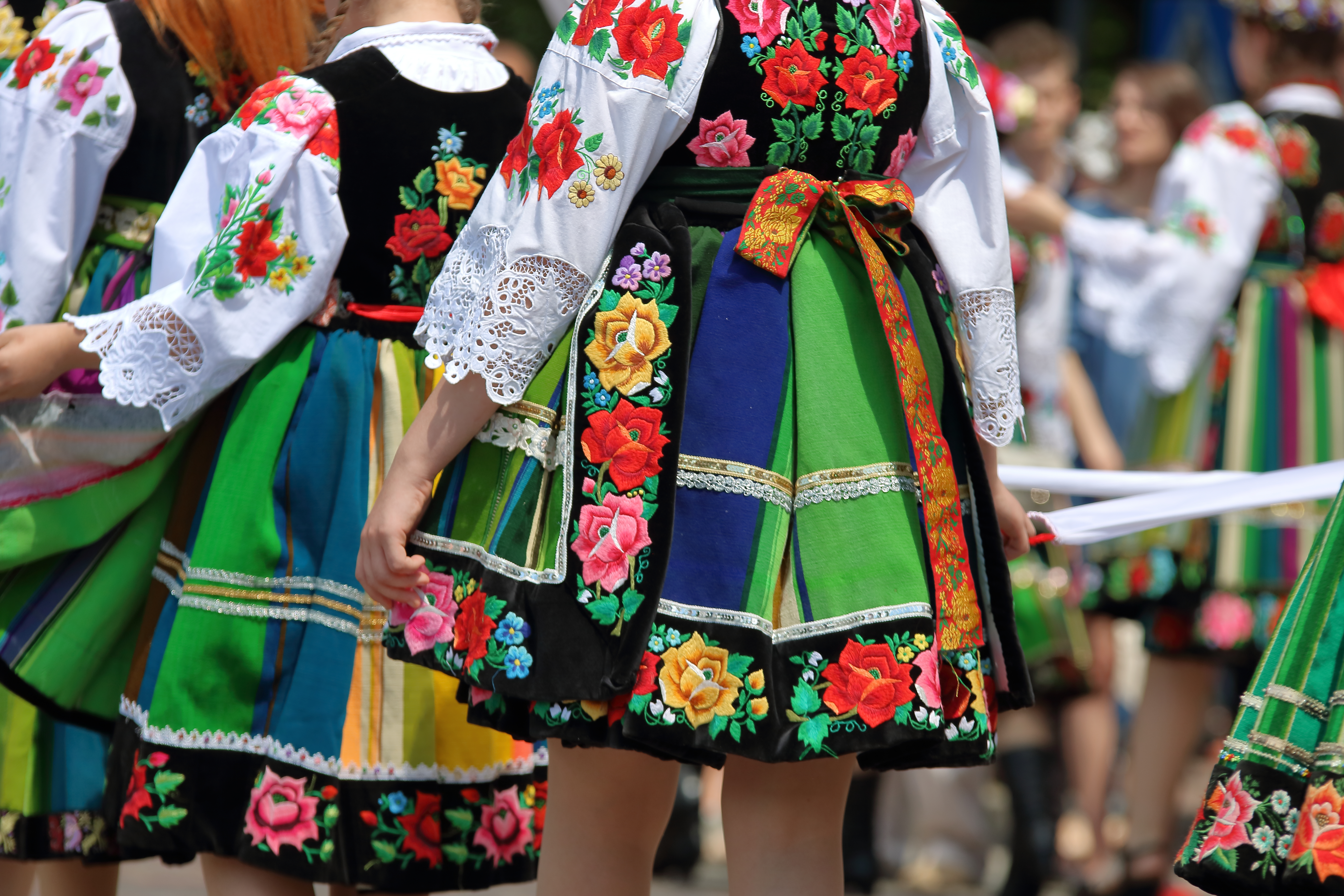 Unge kvinder i farvestrålende stribede folkedragter fra Lowicz-regionen i Polen, fotograferet bagfra under den traditionelle Corpus Christi-procession med blomstermønstre og bånd