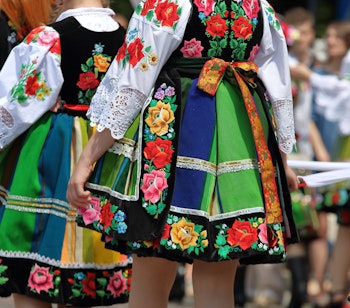Unge kvinder i farvestrålende stribede folkedragter fra Lowicz-regionen i Polen, fotograferet bagfra under den traditionelle Corpus Christi-procession med blomstermønstre og bånd