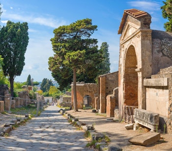 Antikke romerske ruiner i Pompeii med stenbro og søjler under blå himmel