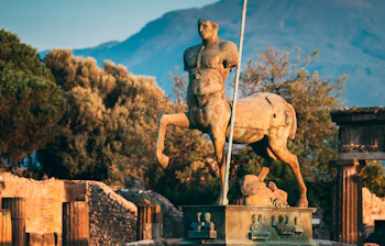 Antik centaur statue i Pompeii med historiske ruiner og Vesuvius i baggrunden