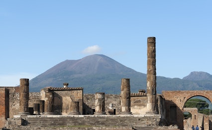 De antikke ruiner af Pompeji med velbevarede søjler og bygninger i forgrunden og Vesuv-vulkanen, der ødelagde den romerske by i år 79, i baggrunden nær Napoli, Italien