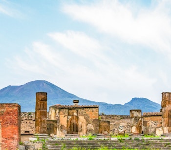 De historiske ruiner af Pompeji med Vesuv-vulkanen i baggrunden, der viser velbevarede romerske søjler og buer fra denne UNESCO-verdensarv nær Napoli