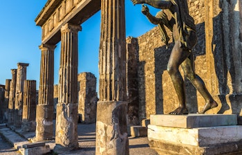 Antikke søjler og bronzestatue i Pompeji ved solnedgang, den historiske romerske by ødelagt af Vesuvs udbrud