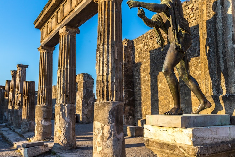 Antikke søjler og bronzestatue i Pompeji ved solnedgang, den historiske romerske by ødelagt af Vesuvs udbrud