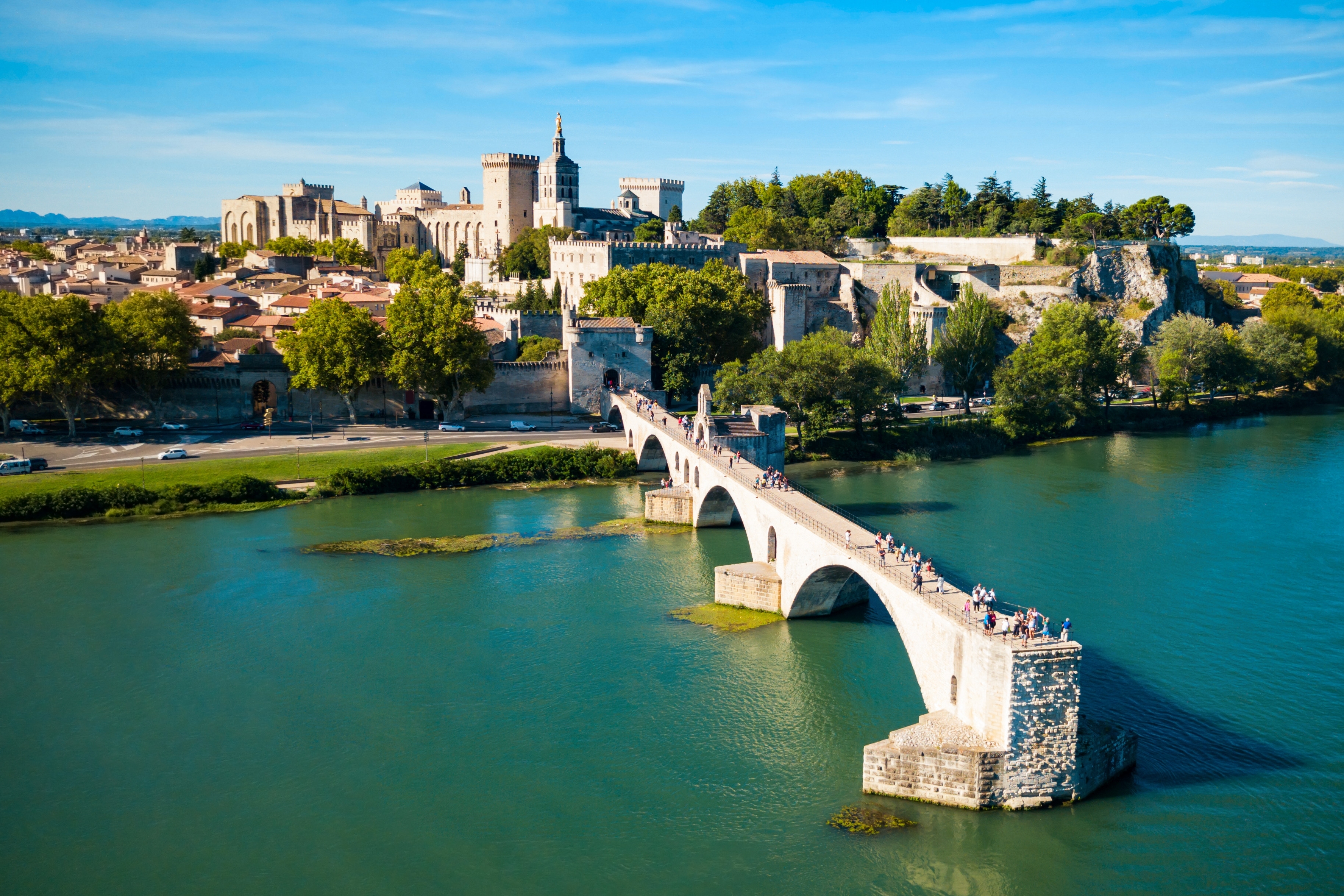 Luftfoto af den historiske Pont Saint-Benezet bro over Rhône-floden i Avignon med middelalderbyen og Pavepaladset i baggrunden under blå himmel