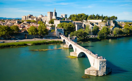 Luftfoto af den historiske Pont Saint-Benezet bro over Rhône-floden i Avignon med middelalderbyen og Pavepaladset i baggrunden under blå himmel