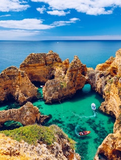 Betagende udsigt over de gyldne klippeformationer ved Ponta da Piedade nær Lagos i Algarve, Portugal, med turkisblåt hav og turistbåd der sejler langs kysten