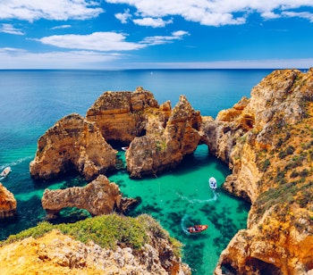 Betagende udsigt over de gyldne klippeformationer ved Ponta da Piedade nær Lagos i Algarve, Portugal, med turkisblåt hav og turistbåd der sejler langs kysten