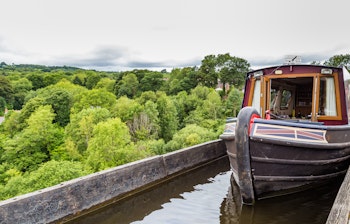 Historisk kanalbåd krydser Pontcysyllte Akvædukten i Wales - verdens højeste akvædukt designet af Thomas Telford med udsigt over den grønne Llangollen-dal