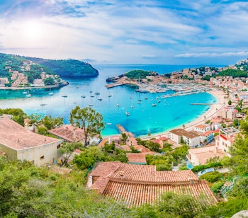 Panoramaudsigt over den idylliske havn i Port de Soller på Mallorca med farverige både og bjerglandskab