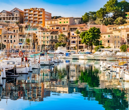 Malerisk udsigt over Port de Sollers hyggelige havn med traditionelle bygninger og sejlbåde ved Middelhavets azurblå vand på Mallorca