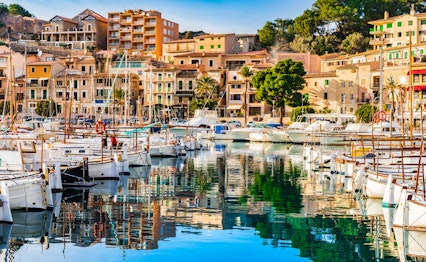 Malerisk udsigt over Port de Sollers hyggelige havn med traditionelle bygninger og sejlbåde ved Middelhavets azurblå vand på Mallorca