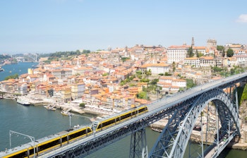 Den ikoniske Dom Luiz bro over Douro-floden med Portos farverige historiske bydel i baggrunden ved solnedgang, Portugal