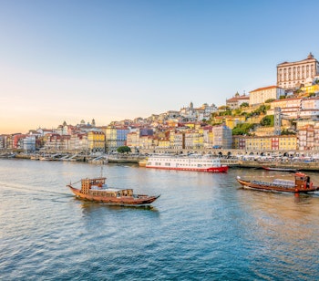 Malerisk udsigt over Portos historiske Ribeira-kvarter med farverige bygninger og både på Douro-floden i gyldent solnedgangslys på haverejse til Nordportugal