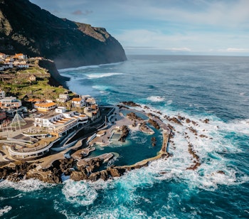 Luftfoto af Porto Moniz med naturlige vulkanske svømmebassiner på Madeira, hvor det krystalklare Atlanterhav møder de dramatiske klipper og skaber unikke bademuligheder