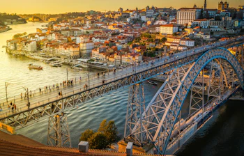 Betagende natvisning af Portos historiske Ribeira-kvarter med farverige oplyste bygninger langs Douro-floden og den ikoniske Ponte Dom Luis bro, der skinner i aftenmørket