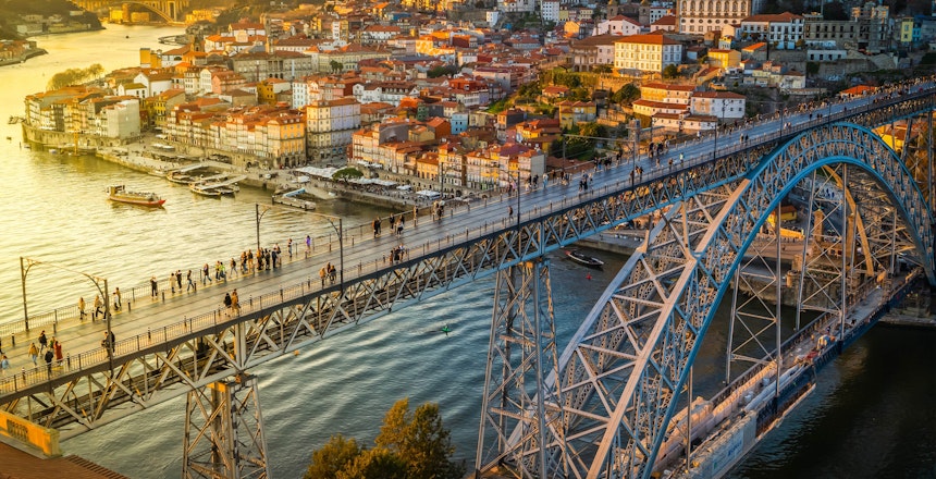 Betagende natvisning af Portos historiske Ribeira-kvarter med farverige oplyste bygninger langs Douro-floden og den ikoniske Ponte Dom Luis bro, der skinner i aftenmørket