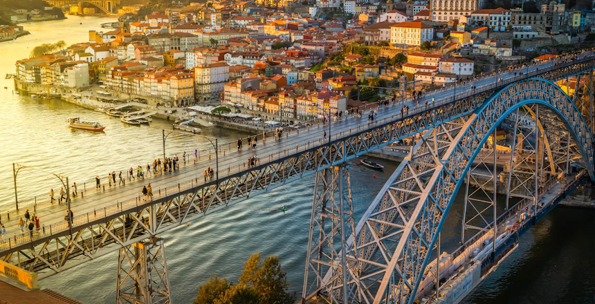 Betagende natvisning af Portos historiske Ribeira-kvarter med farverige oplyste bygninger langs Douro-floden og den ikoniske Ponte Dom Luis bro, der skinner i aftenmørket