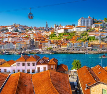 Betagende panoramaudsigt over Porto i Portugal på en solrig sommerdag med byens farverige bygninger, røde tegltage, Douro-floden med både og den ikoniske bro over vandet