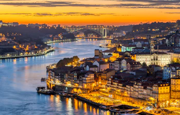 Luftudsigt over Portos gamle bydel Ribeira med den gyldne solnedgang reflekteret i Douro-floden og den oplyste havnefront i Portugal