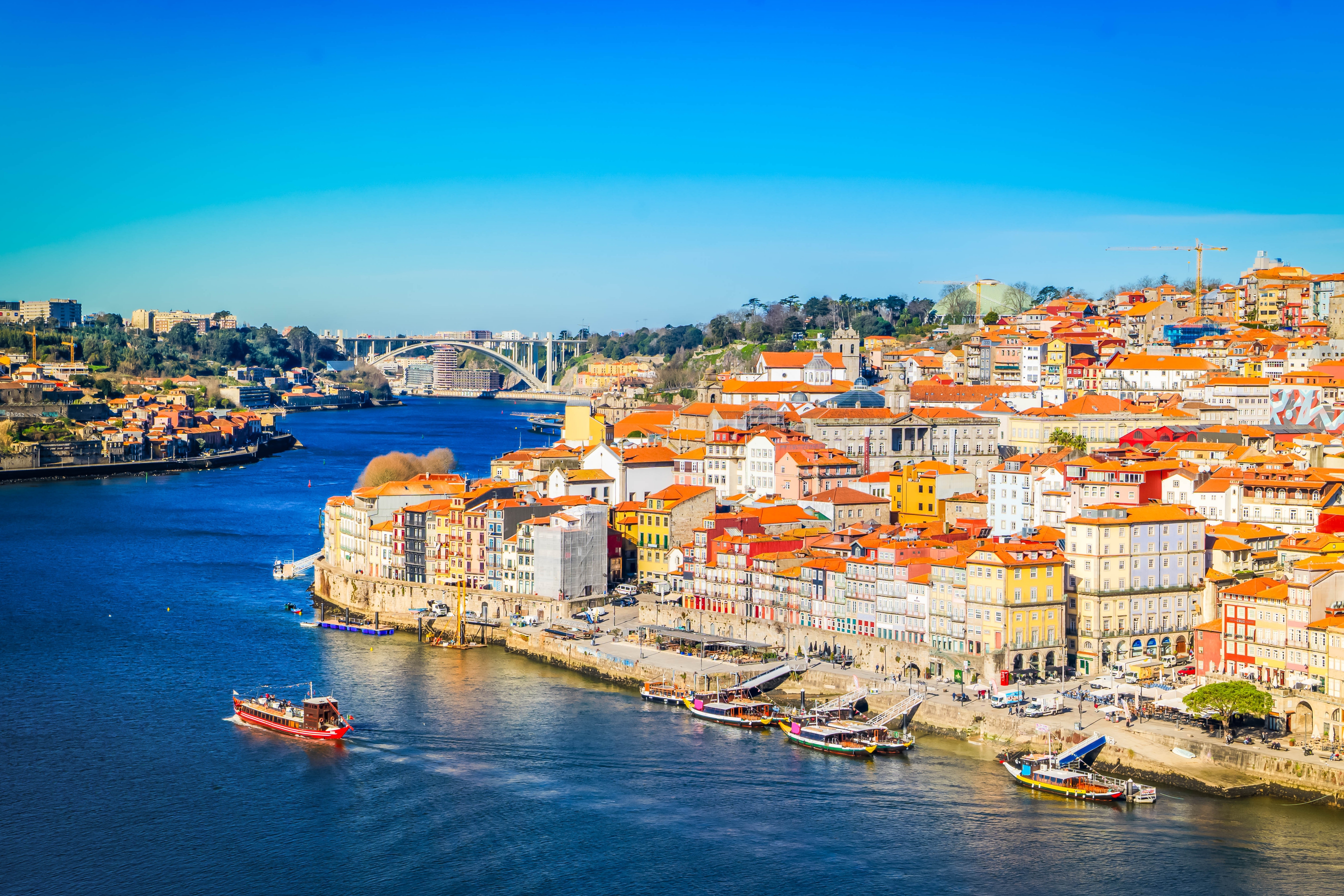 Farverig udsigt over Portos historiske Ribeira-kvarter langs Douro-floden med traditionelle både og røde tagtegl i solskin